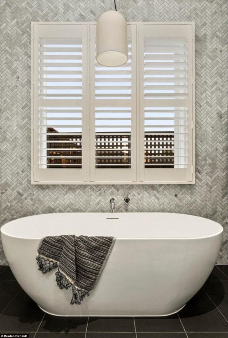 Bathroom with white tub, shutters, herringbone tile, and a hanging light.