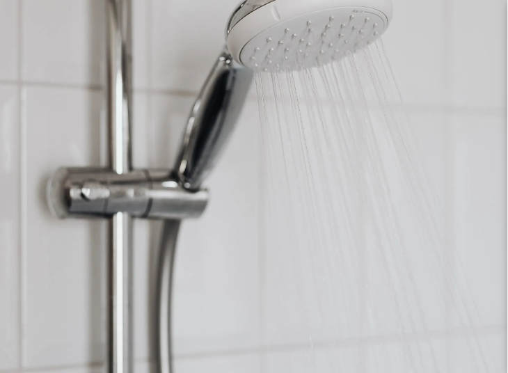 Shower head spraying water against a white-tiled wall.