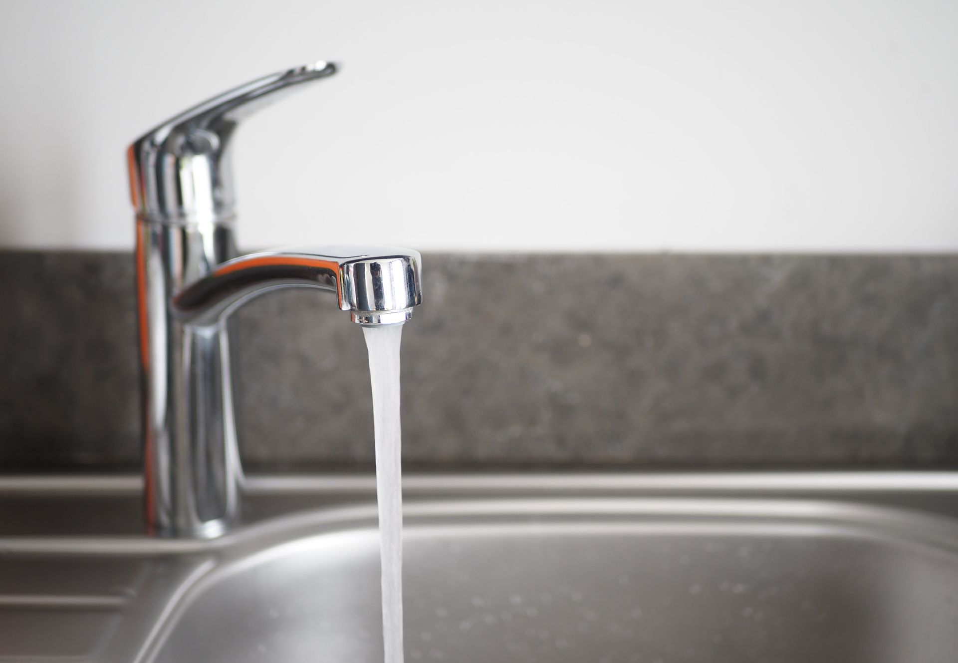 Faucet with running water over a stainless steel sink in a kitchen setting.