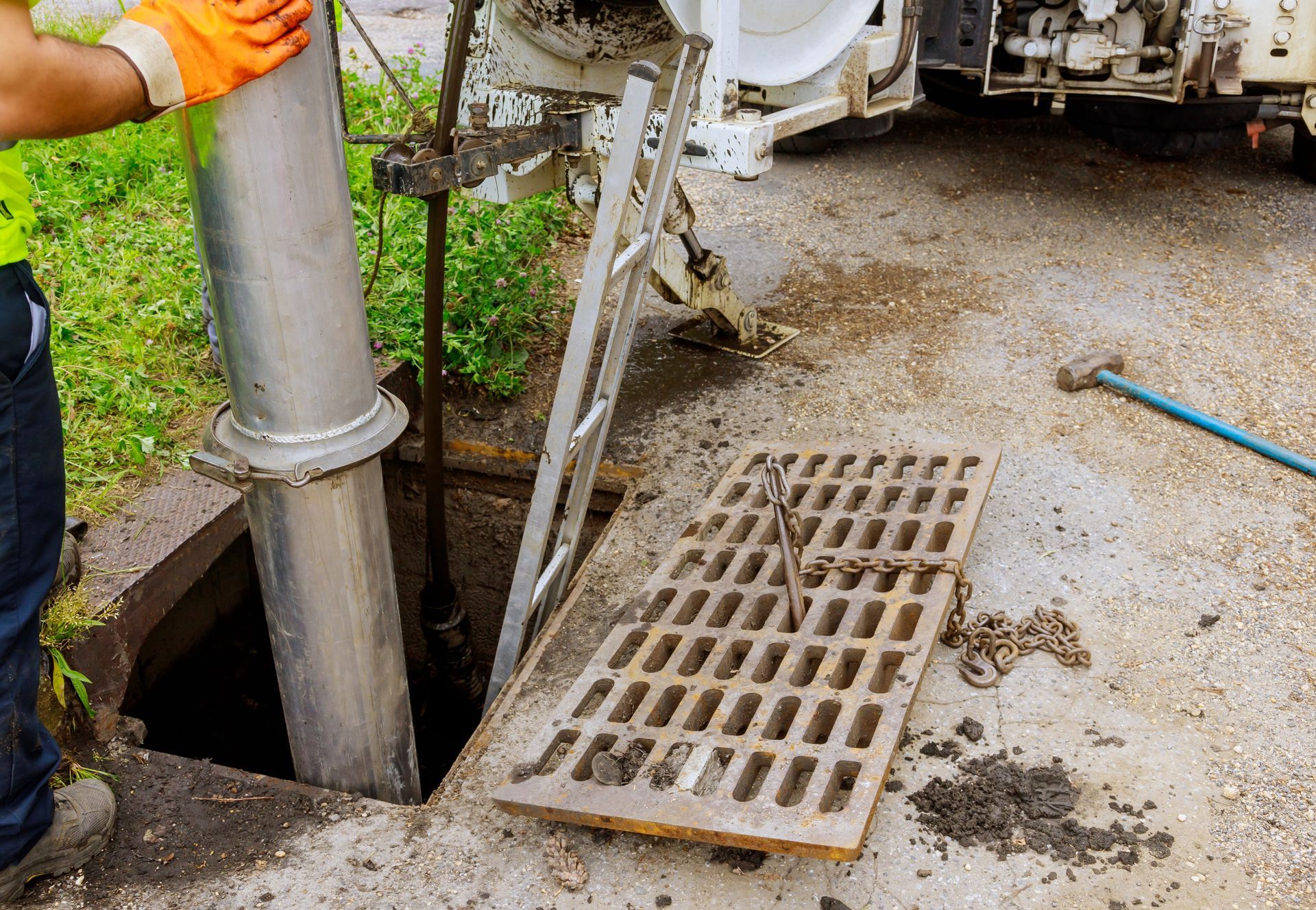 Man working on a sewer. Holds a metal pipe over an open manhole. Orange gloves.