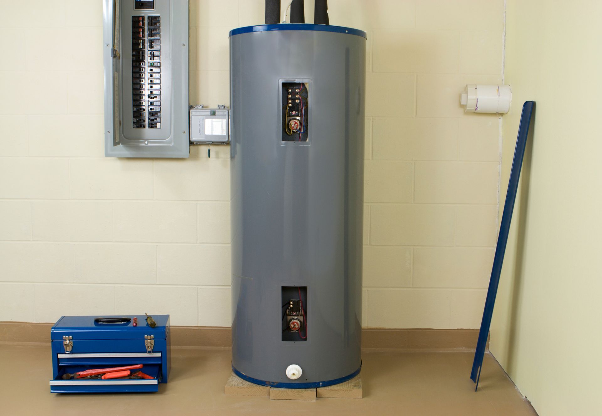 A water heater with electrical panel and toolbox in a utility room.