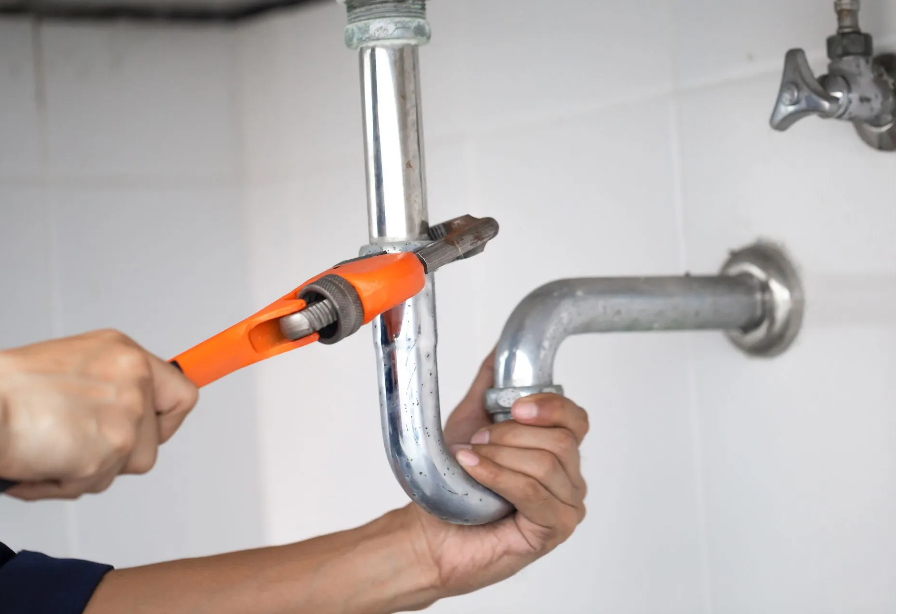 Plumber using a wrench to loosen a pipe under a sink.