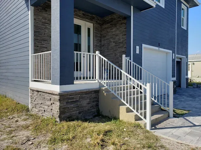 Exterior of a blue house with a porch and steps featuring white railings, stone facade, and a garage door.