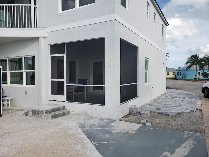 Exterior view of a two-story light gray building with a screened porch and stone patio area.