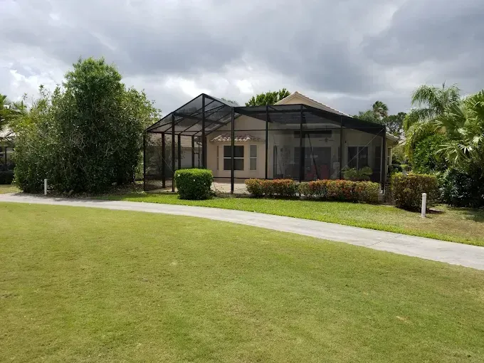 House with screened patio, surrounded by green grass and pathway, cloudy sky.