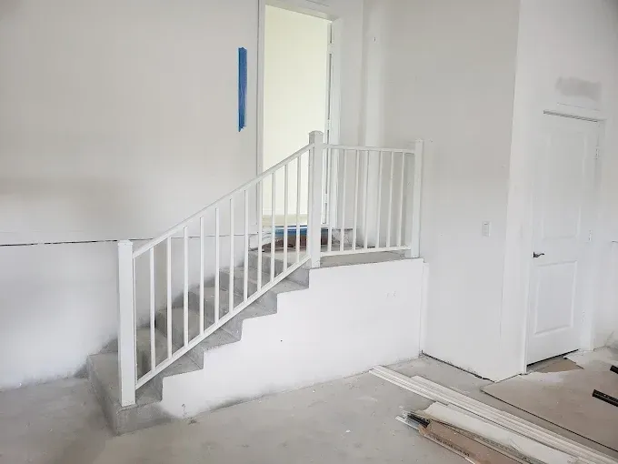 White painted stairs with a railing lead to a doorway and a white door in an unfinished room.