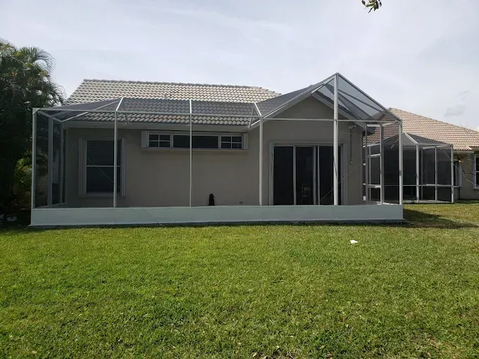 White screened-in patio attached to a light-colored house with a tiled roof. Green grass lawn in foreground.