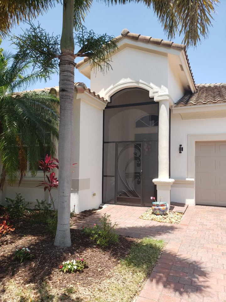 White house with screened front door, brick path, palm tree, and lush landscaping.