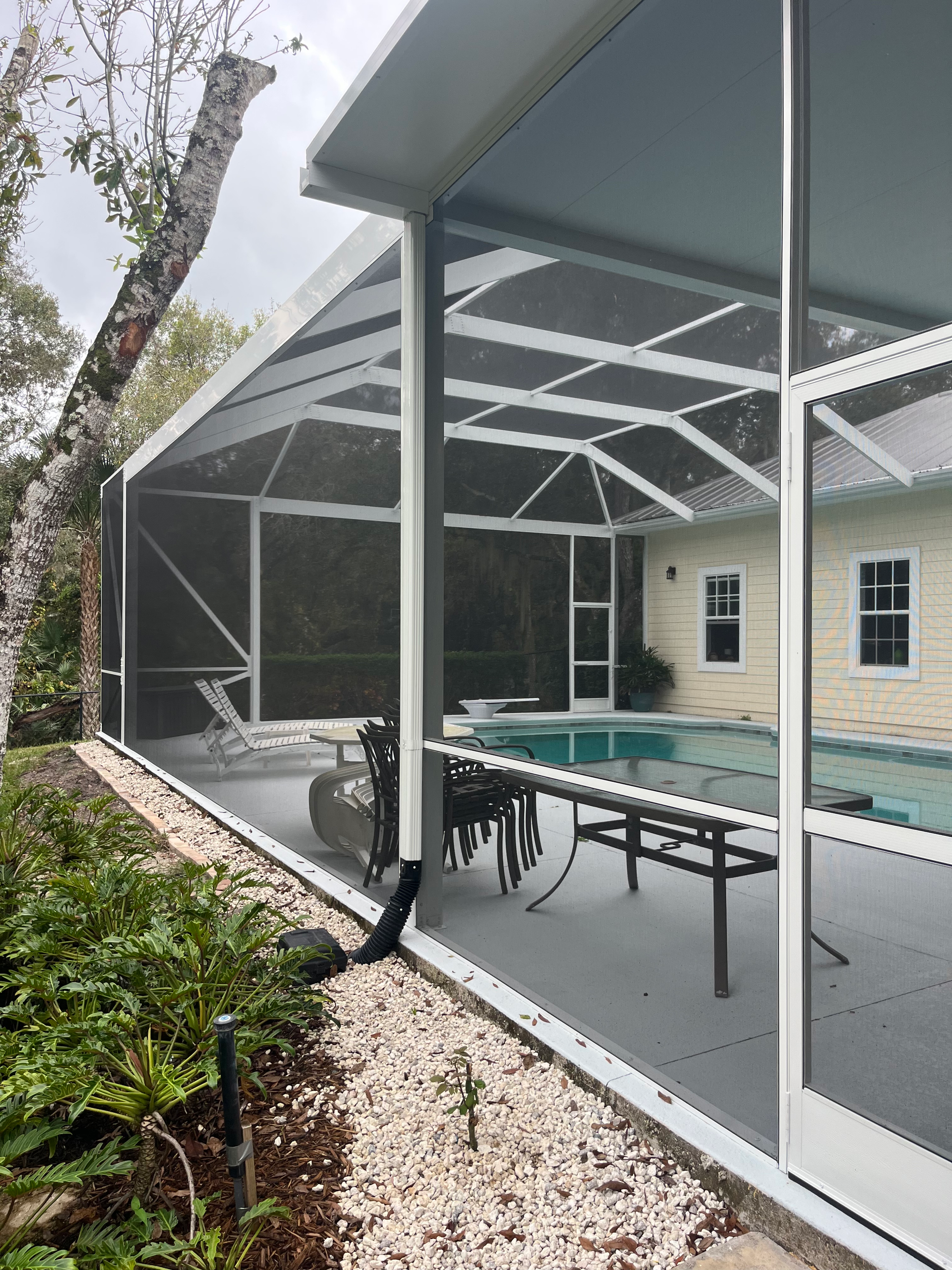 Person on a ladder cleaning a white screen enclosure frame next to a pool.