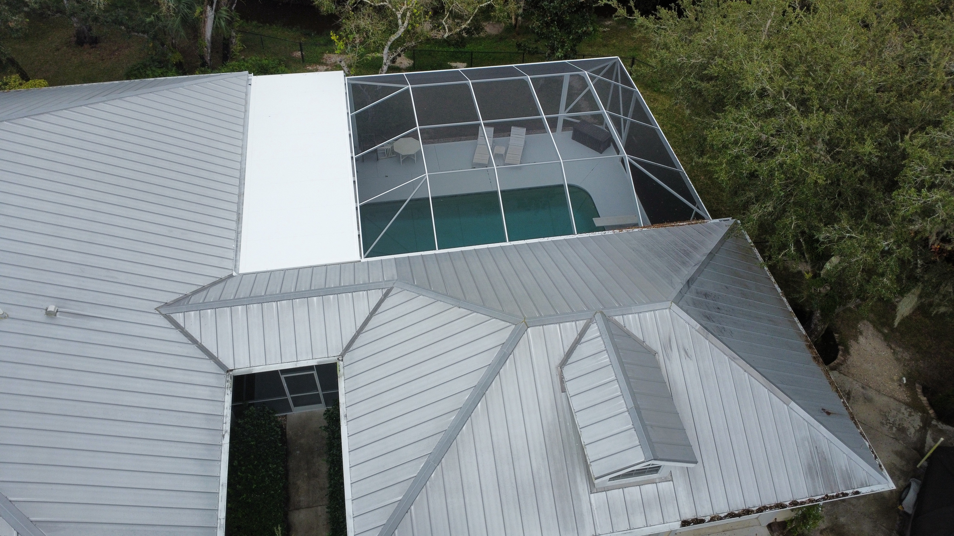 Overhead view of a house with a pool enclosed in a screened structure. Gray roof, green yard.