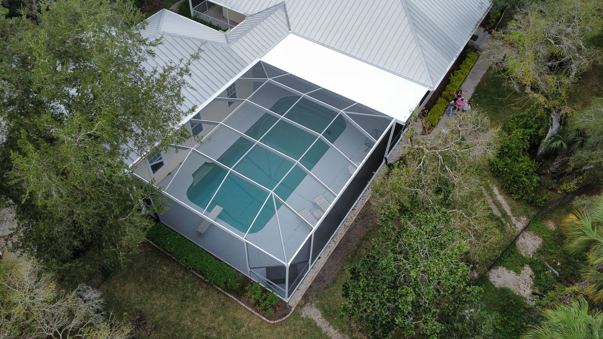Overhead view of a house with a screened-in pool, surrounded by trees and green foliage.