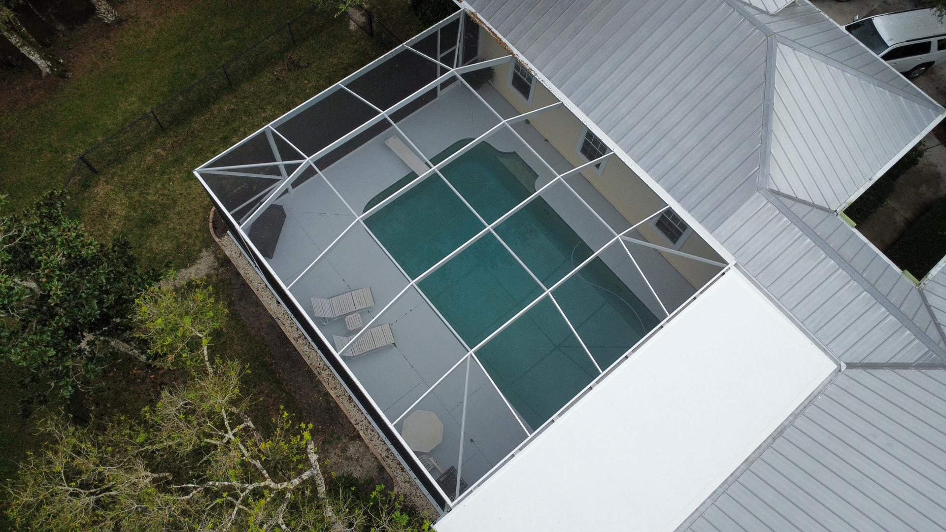 Overhead view of a swimming pool enclosed in a screened patio, adjacent to a home with a gray roof.