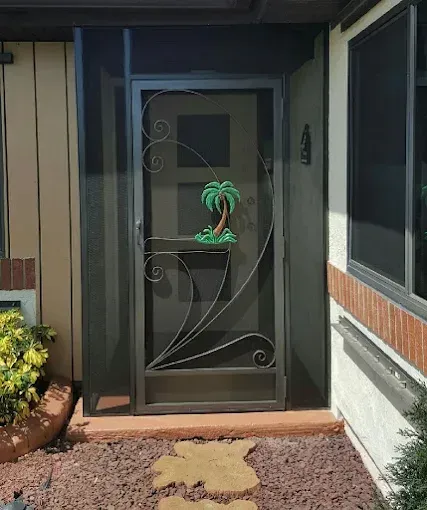 Dark metal screen door with decorative scrollwork, a small palm tree, and a screen enclosure.