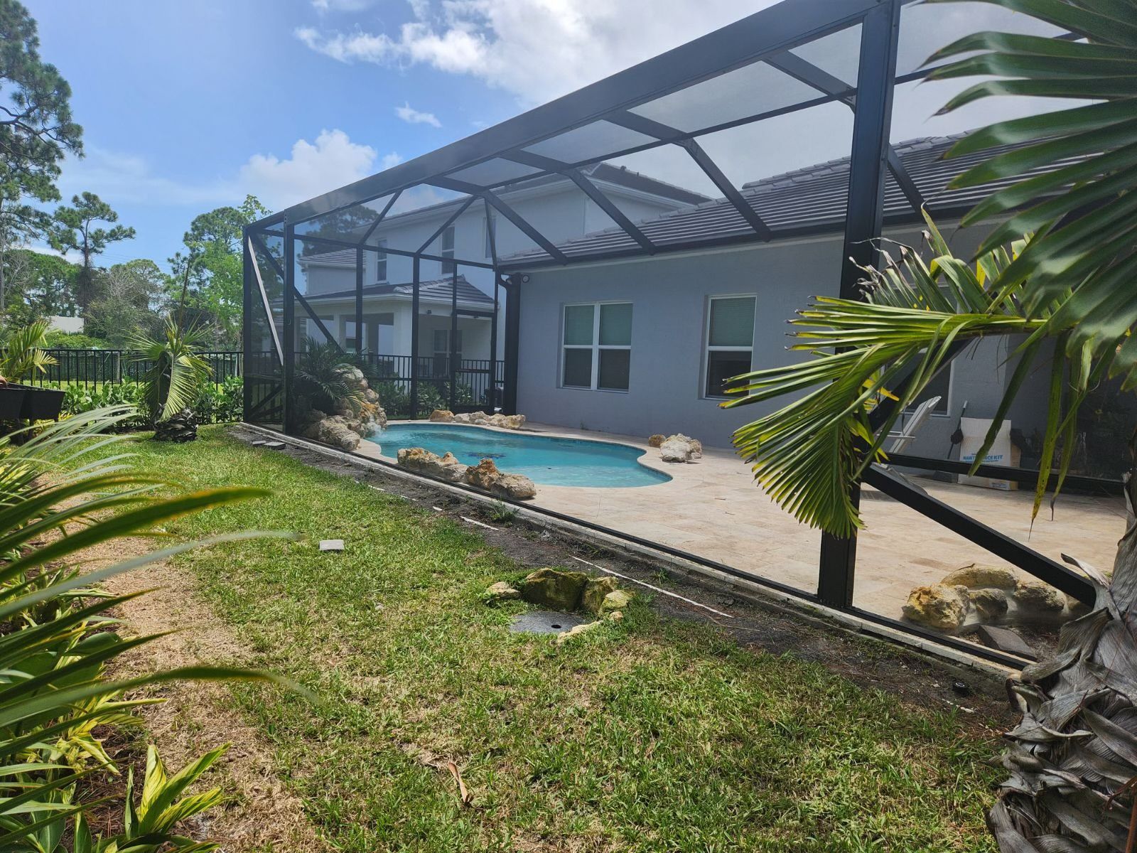 Backyard with screened pool, light blue siding, lush greenery, and bright sky.