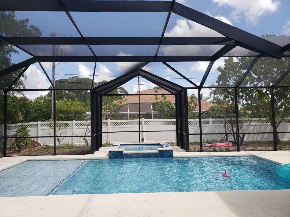 Pool and jacuzzi under a screened enclosure. Clear blue water, black framing, and a sunny sky.