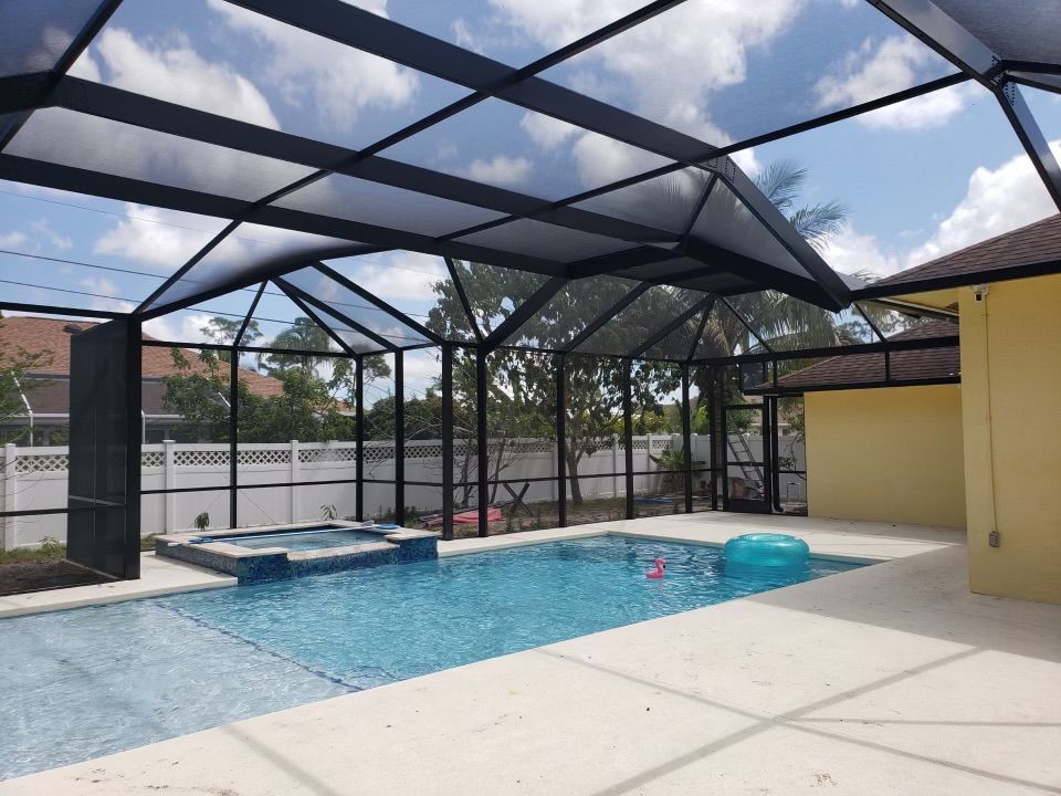 Pool enclosure with a swimming pool and spa. Black metal frame with a glass roof.