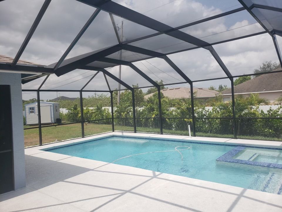 Pool enclosed by black screening, set in backyard under a cloudy sky.