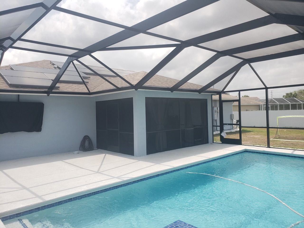 Pool area with a screened enclosure. Pool is blue with a white patio. The structure is gray and black.