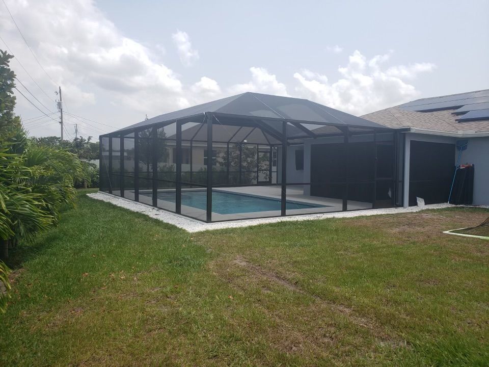 Pool enclosed in black screen structure, house with solar panels in background. Green grass and blue sky.