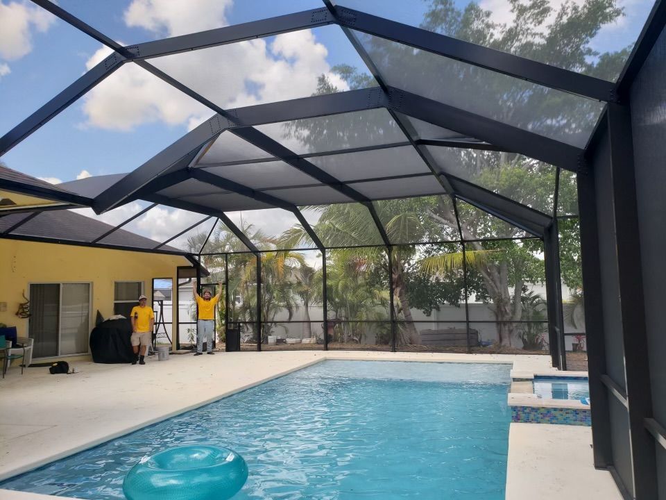 Pool enclosed by a black screen structure under a sunny sky; two people work near pool.