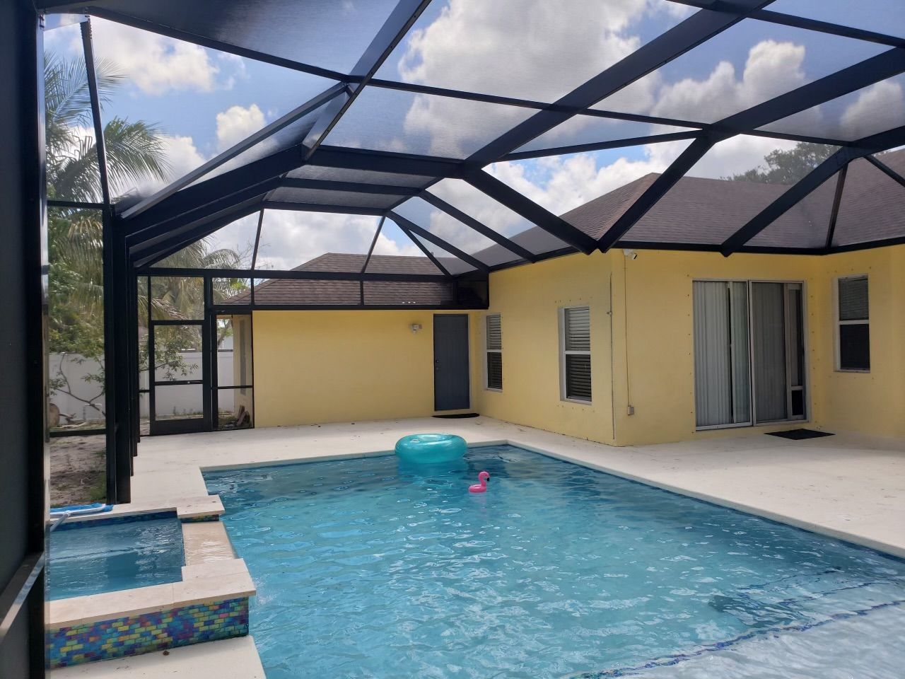 Pool area with screen enclosure; pool, jacuzzi, yellow house, and blue inflatable.