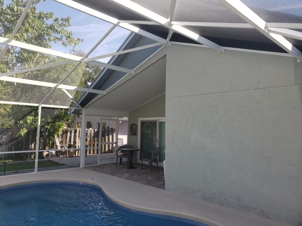 Pool with screened enclosure attached to a light green stucco house.