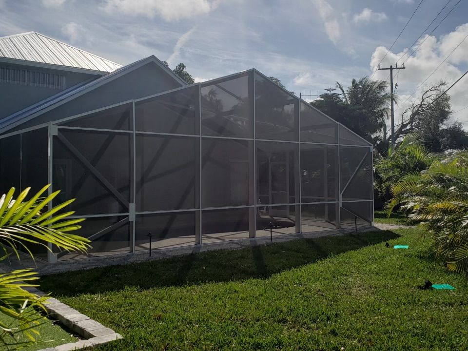 Screened-in patio extension attached to a house; gray screen walls, green grass, sunny day.