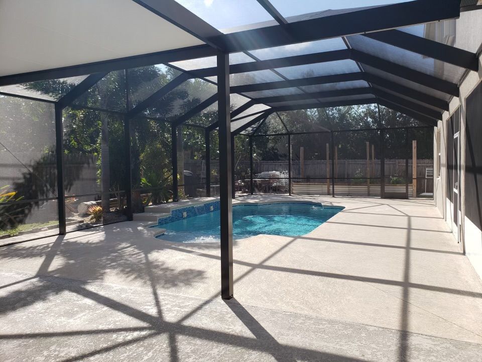 A screened-in patio with a pool. Dark metal frame with a transparent roof and concrete deck.