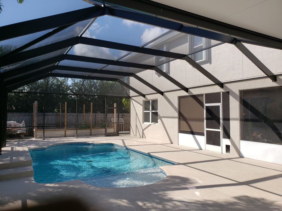 Pool enclosed in screened structure, black frame, turquoise water, adjacent to house with concrete patio.
