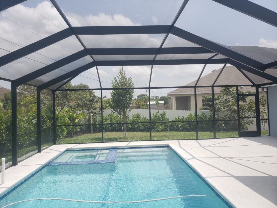 Swimming pool under a black screened enclosure with a blue pool and spa.