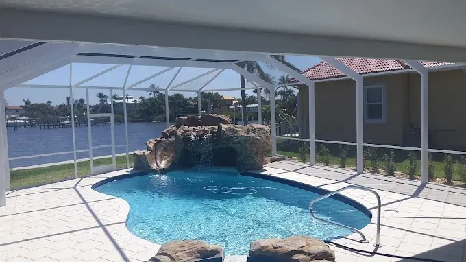 Swimming pool with rock waterfall feature, screened enclosure, overlooking water.
