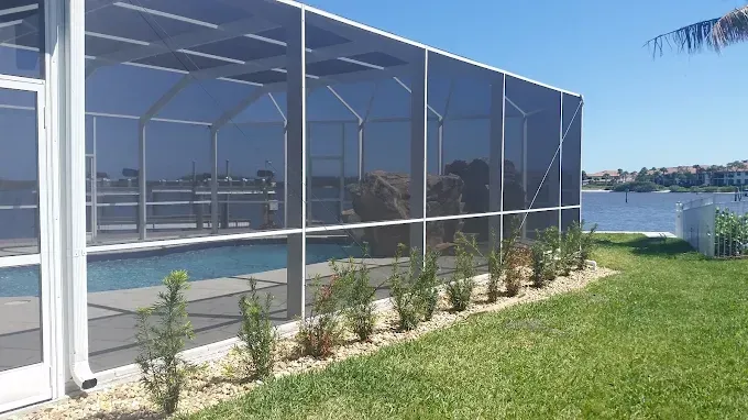 Screened-in pool enclosure with white frame, pool, plants, and water view.