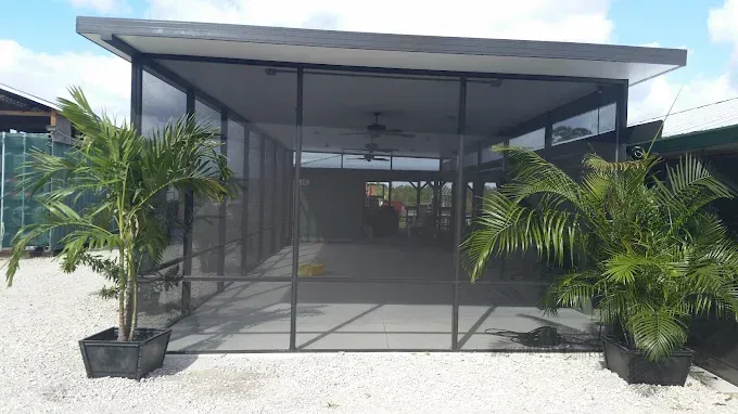 Screened-in patio with palms in planters, a ceiling fan, and a light-colored gravel ground.