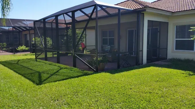 Screened-in patio with black framing attached to a light-colored house. Green grass surrounds it.