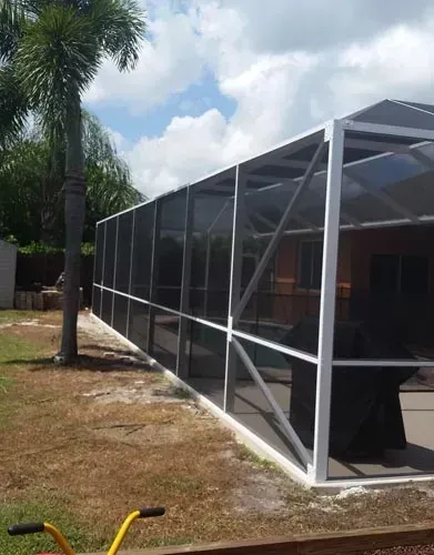 Screened pool enclosure with white frame, on a lawn near a palm tree.
