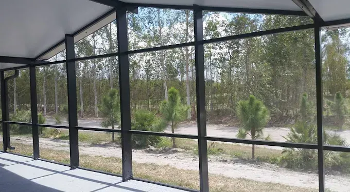 Screened-in porch with black frames, overlooking a treed landscape on a sunny day.