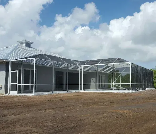 A screened-in porch enclosure with a silver frame, attached to a light gray house under a cloudy sky.