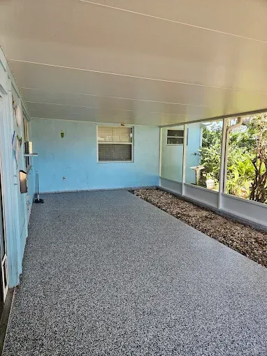 Enclosed porch with gray speckled flooring, light blue walls and ceiling, windows overlooking greenery.