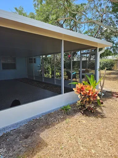 Screened-in porch with light blue walls, gray roof, and stone landscaping.  Bright green plants with orange accents are in the foreground.