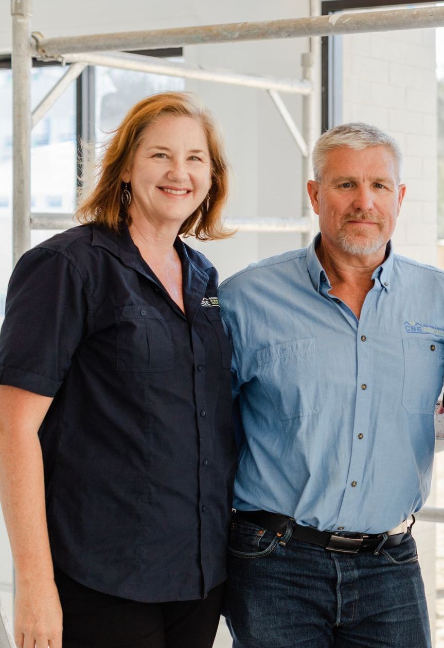 A man and a woman are posing for a picture in front of a scaffolding — Custom Home Builders in the Hunter Valley