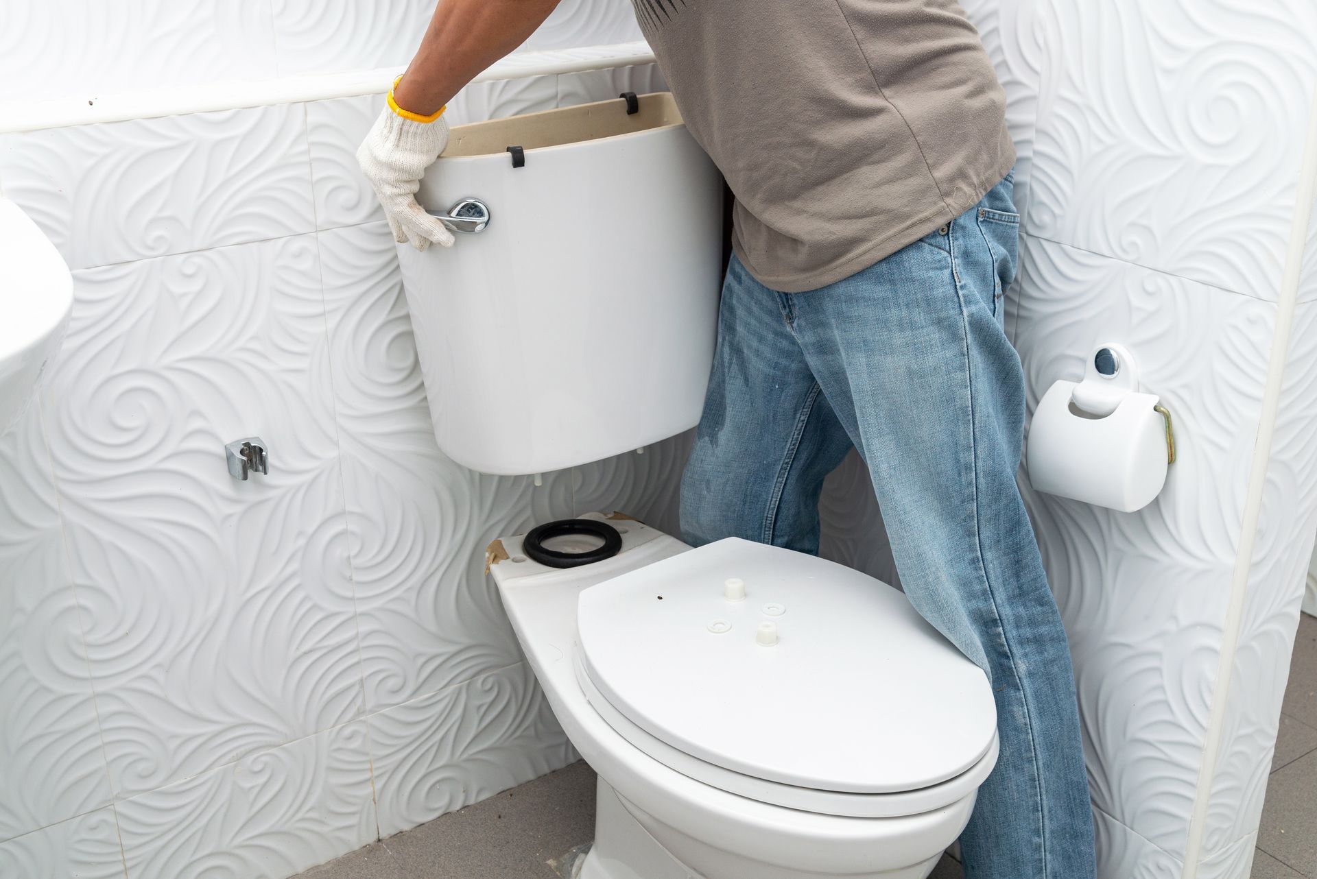 A man is fixing a toilet in a bathroom.
