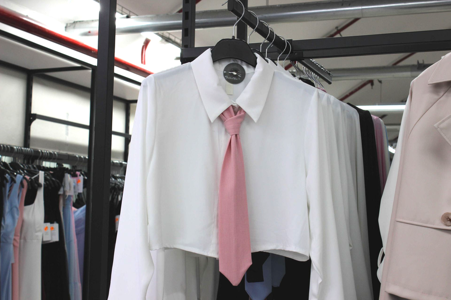 Una camicia bianca corta con bottoni, abbinata a una cravatta rosa, esposta su una gruccia in un negozio di abbigliamento.