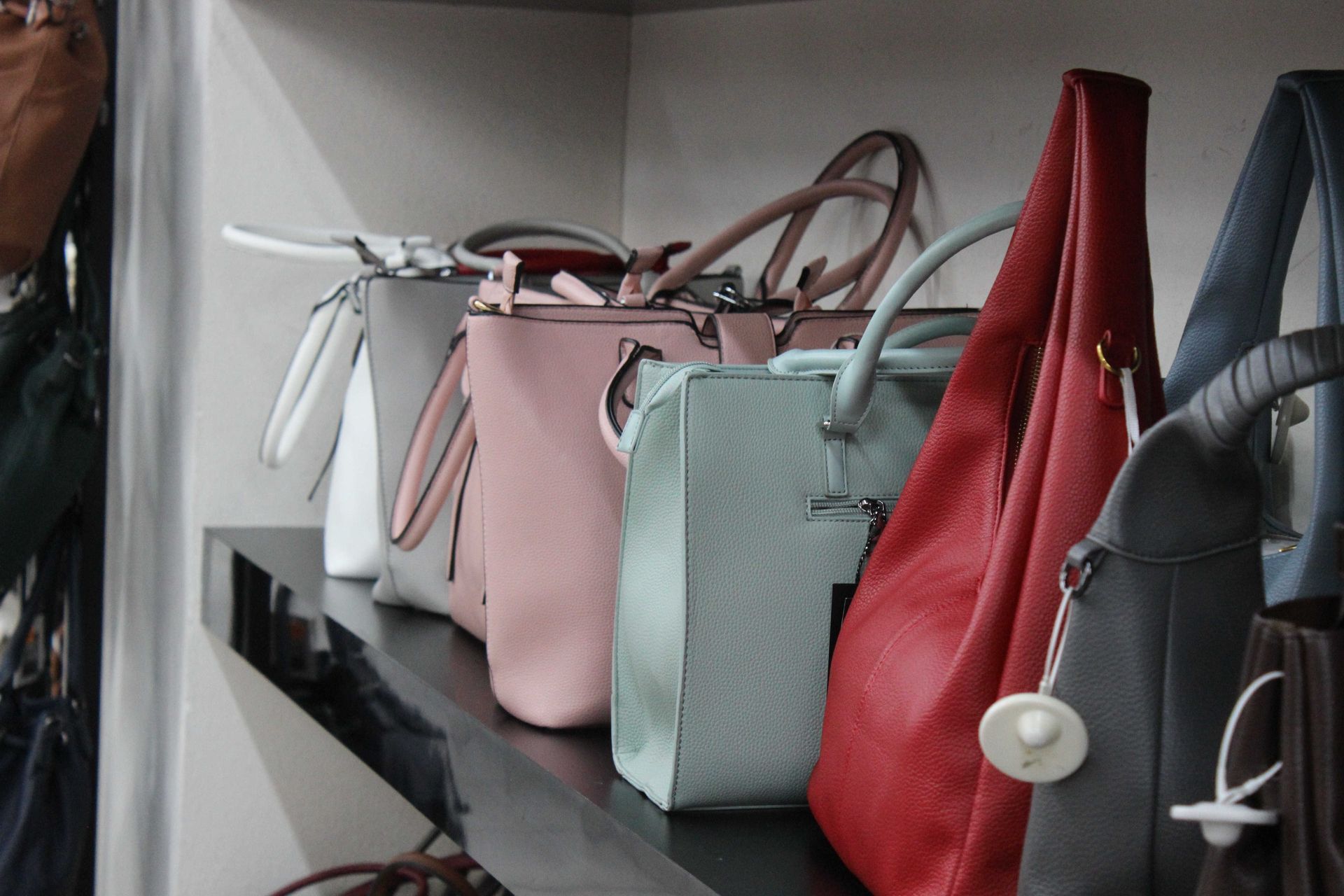 Su uno scaffale è esposta una fila di borse di vari colori, tra cui bianco, grigio, rosa, azzurro, rosso e grigio scuro.