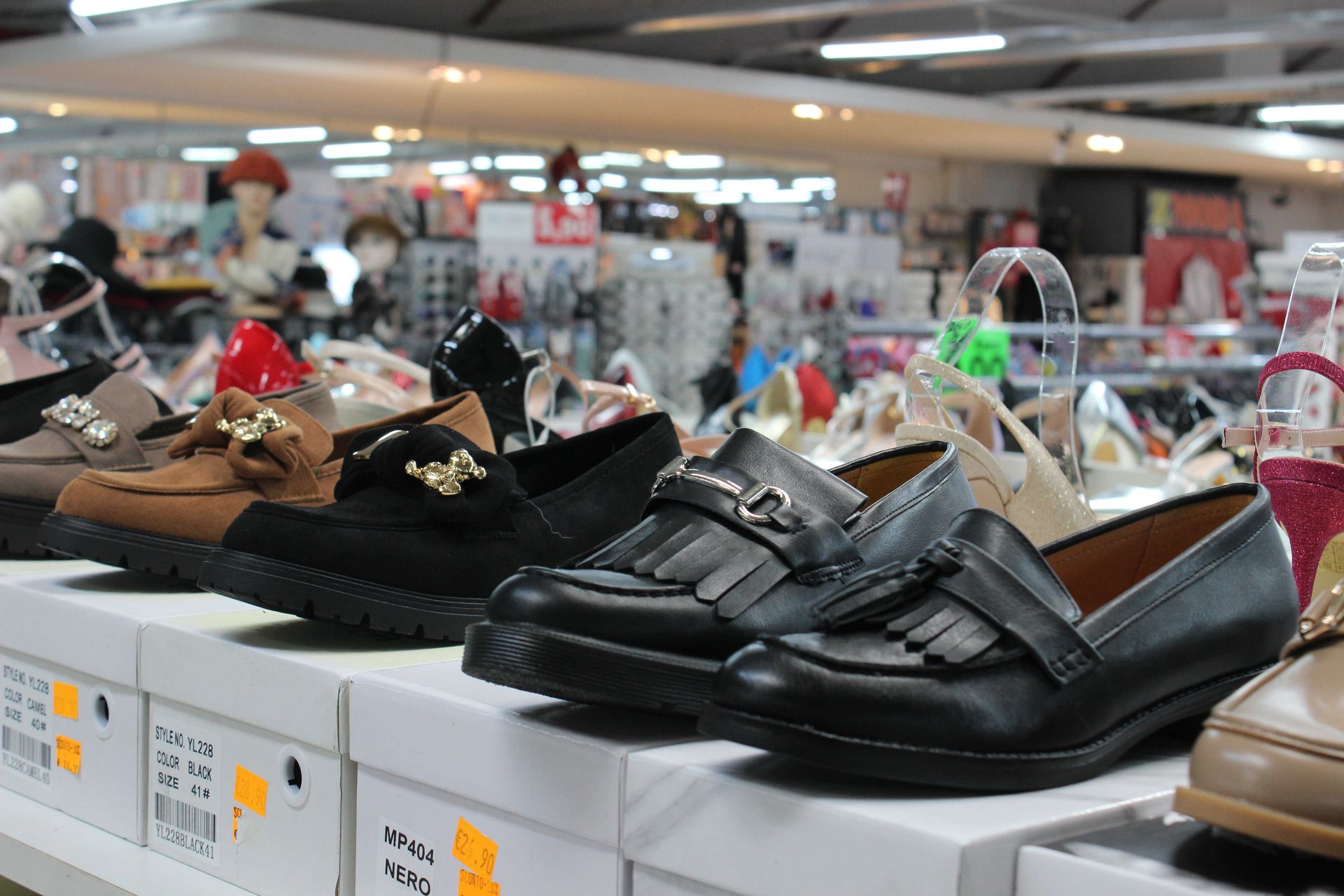 Una vetrina di un negozio che mostra file di mocassini neri e marroni su scatole bianche, con altre calzature visibili sullo sfondo.