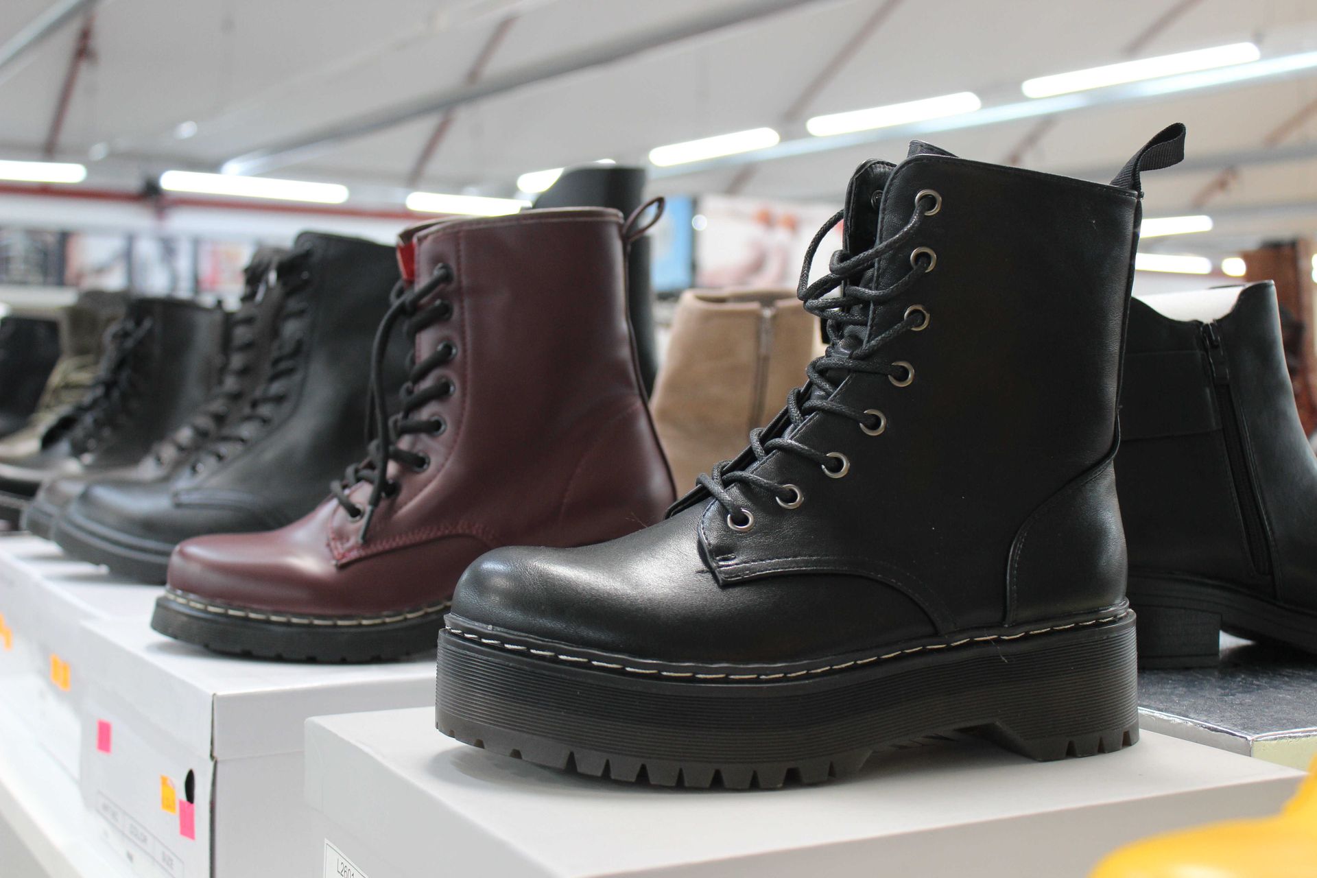 In un negozio, una fila di diversi modelli di stivali da combattimento con lacci è esposta su degli scaffali.