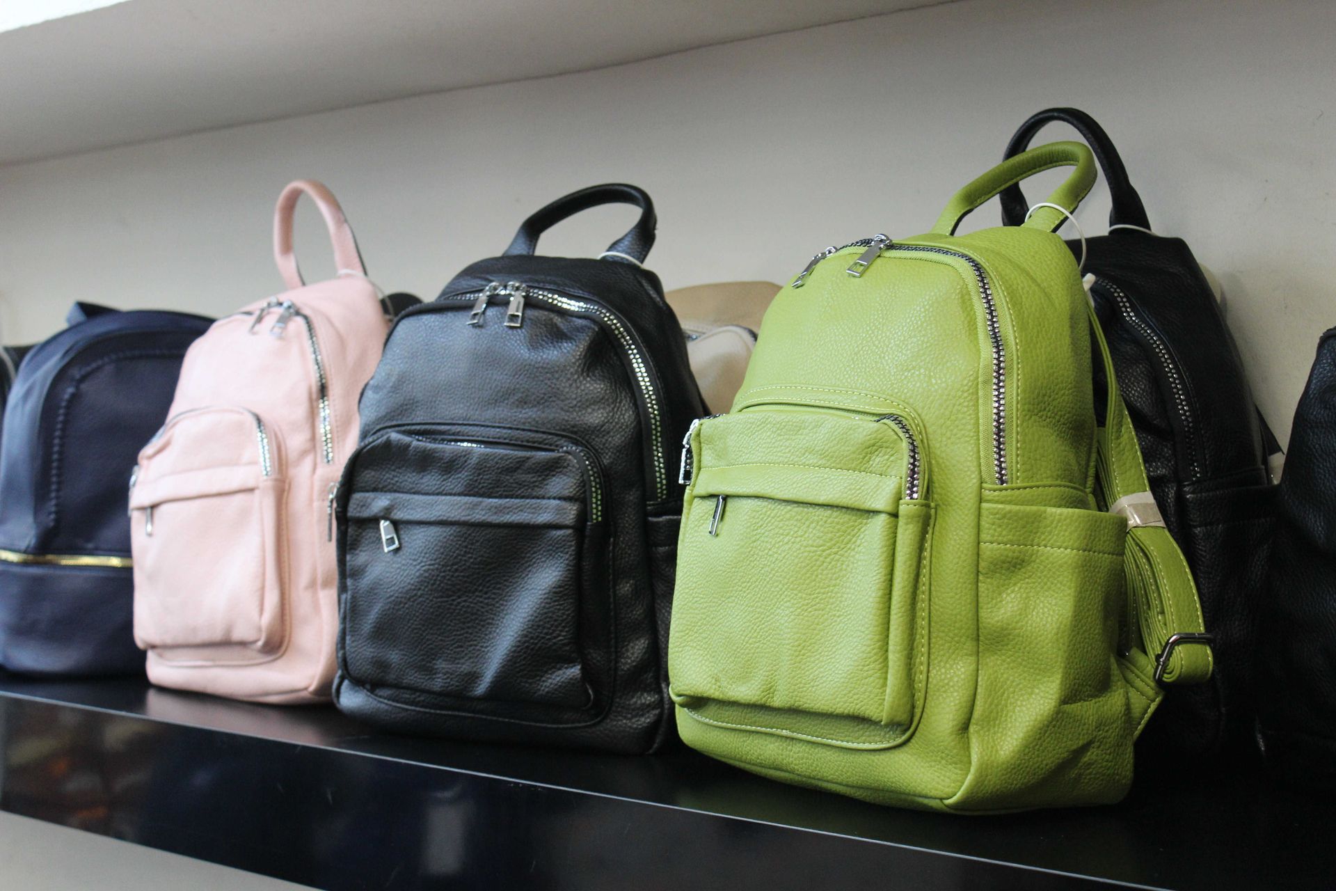 Una fila di zaini in similpelle di vari colori esposti su uno scaffale.