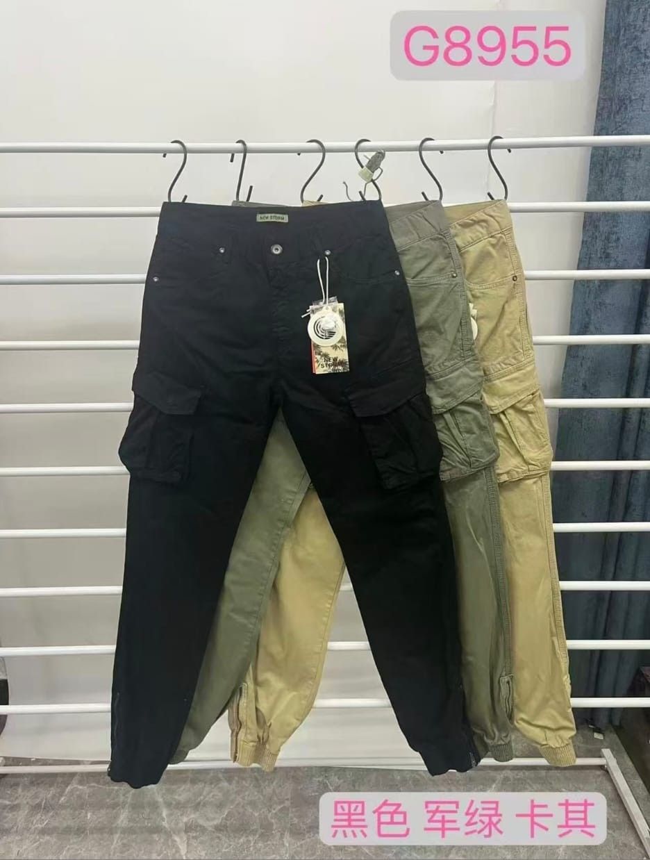 Quattro paia di pantaloni cargo, neri, verde scuro, verde oliva e kaki, sono esposti su grucce, su uno scaffale.