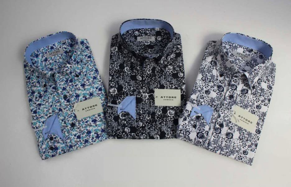 Tre camicie eleganti a fantasia, blu, nere e bianche, piegate e disposte una accanto all'altra su uno sfondo chiaro.