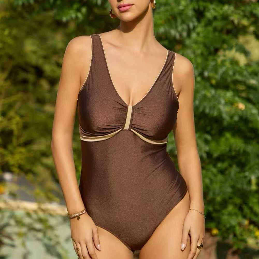 Donna in costume intero marrone in piedi all'aperto, con uno sfondo verde di foglie.