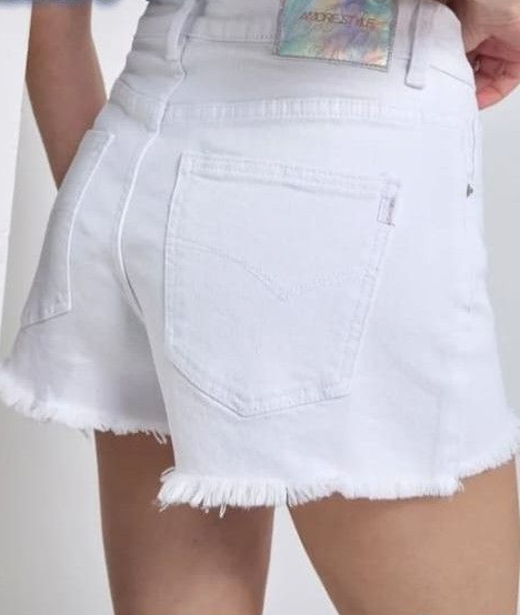 Pantaloncini di jeans bianchi sfrangiati indossati da una persona, vista posteriore, con un top colorato visibile in vita.